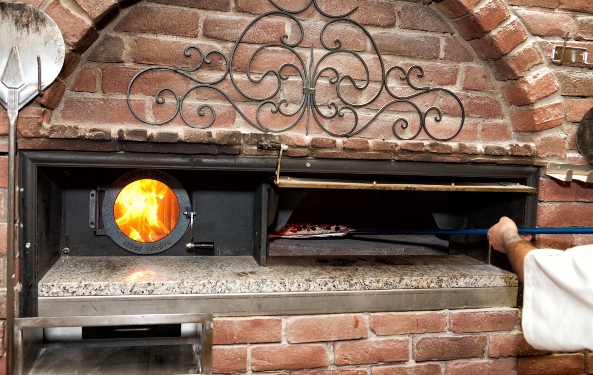 A person is putting a pizza into a brick oven