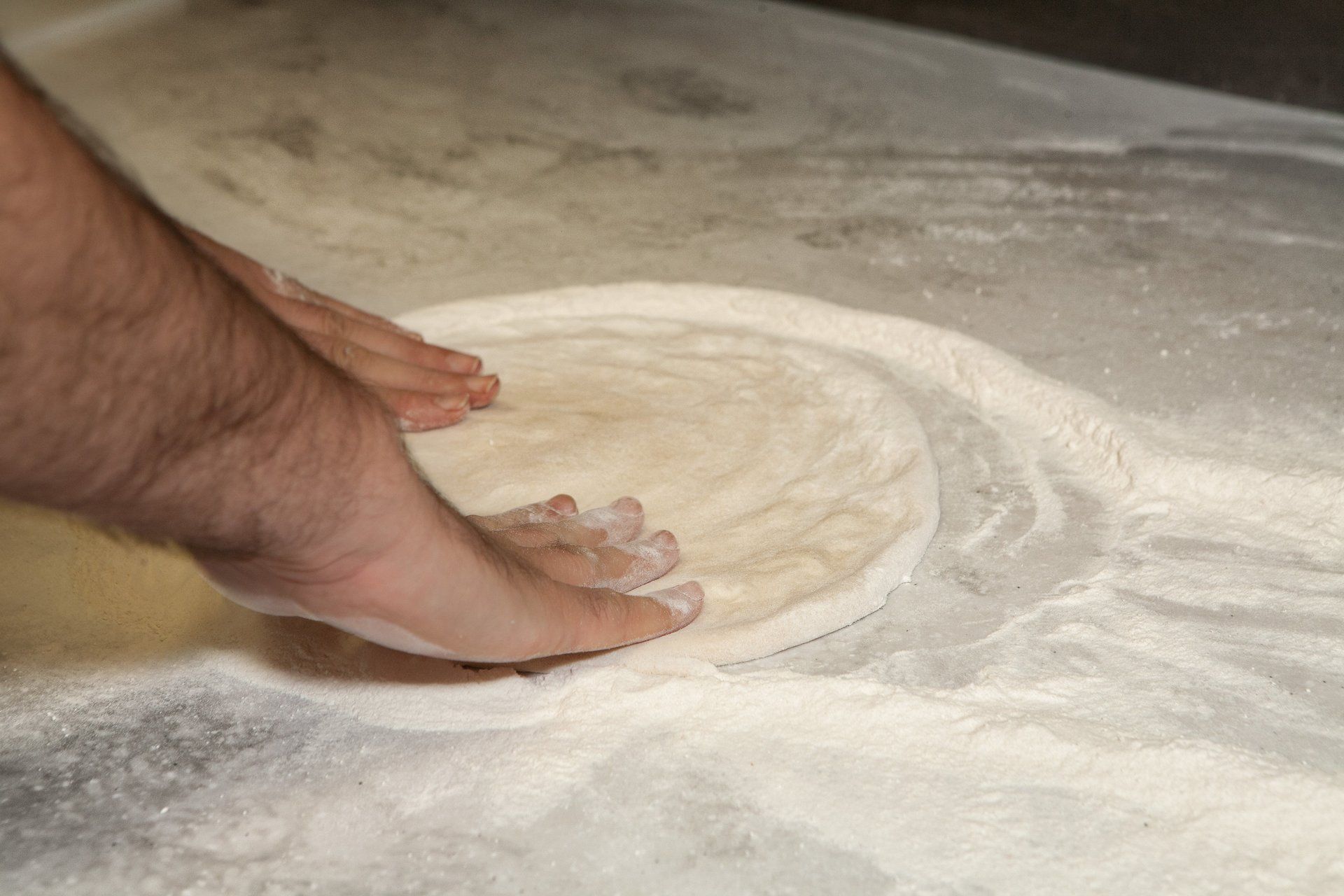 A person 's foot is on a piece of pizza dough