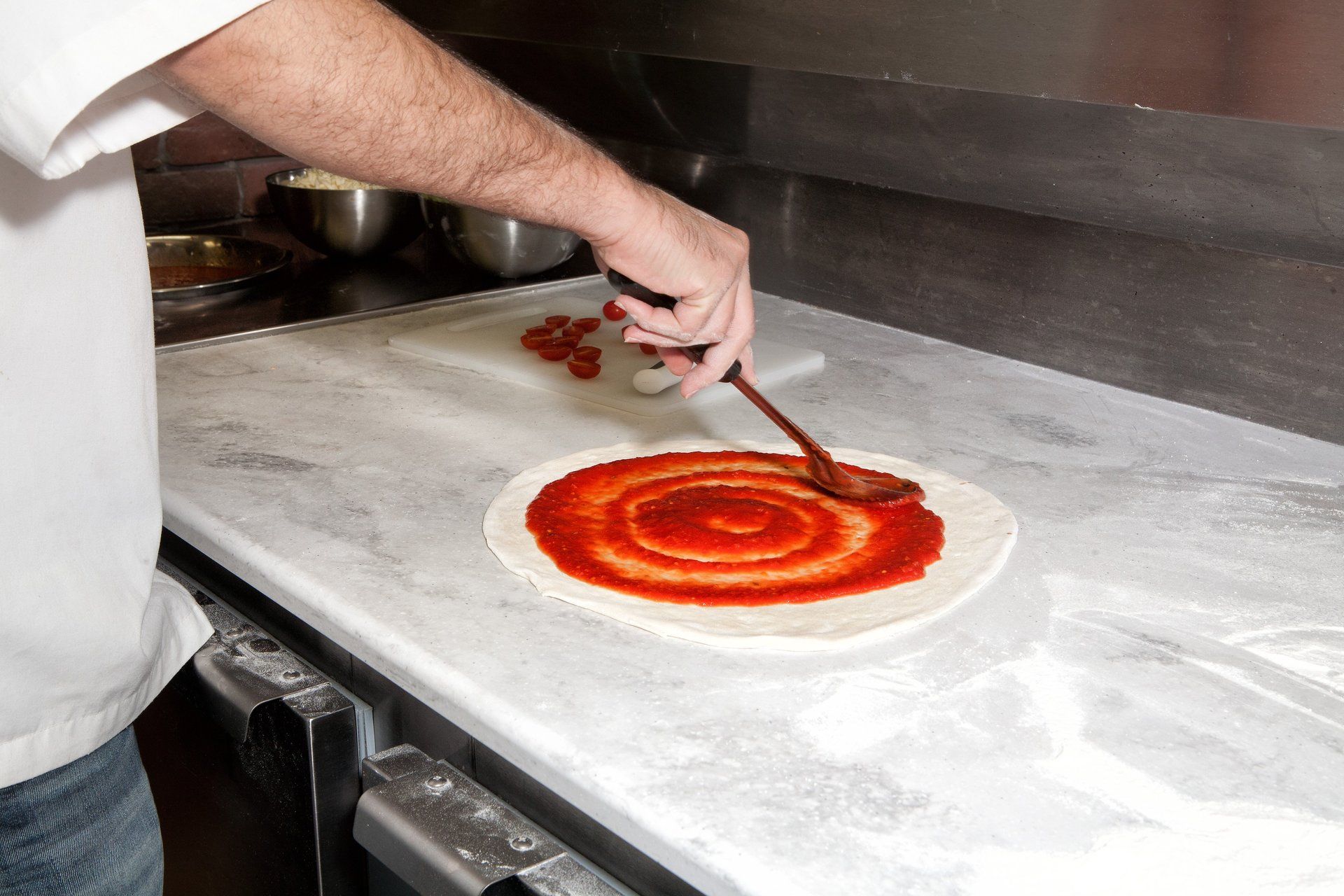 A person is spreading tomato sauce on a pizza