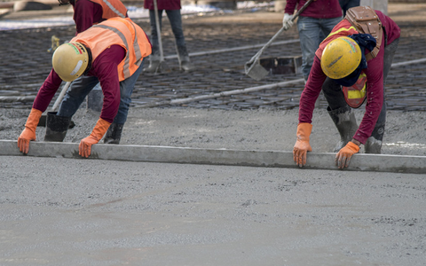 Construction worker troweling wet concrete on a top of concrete floor slab new construction site