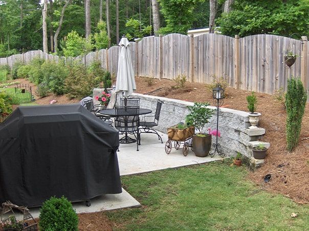 A backyard with a table and chairs and a grill covered in a black cover.