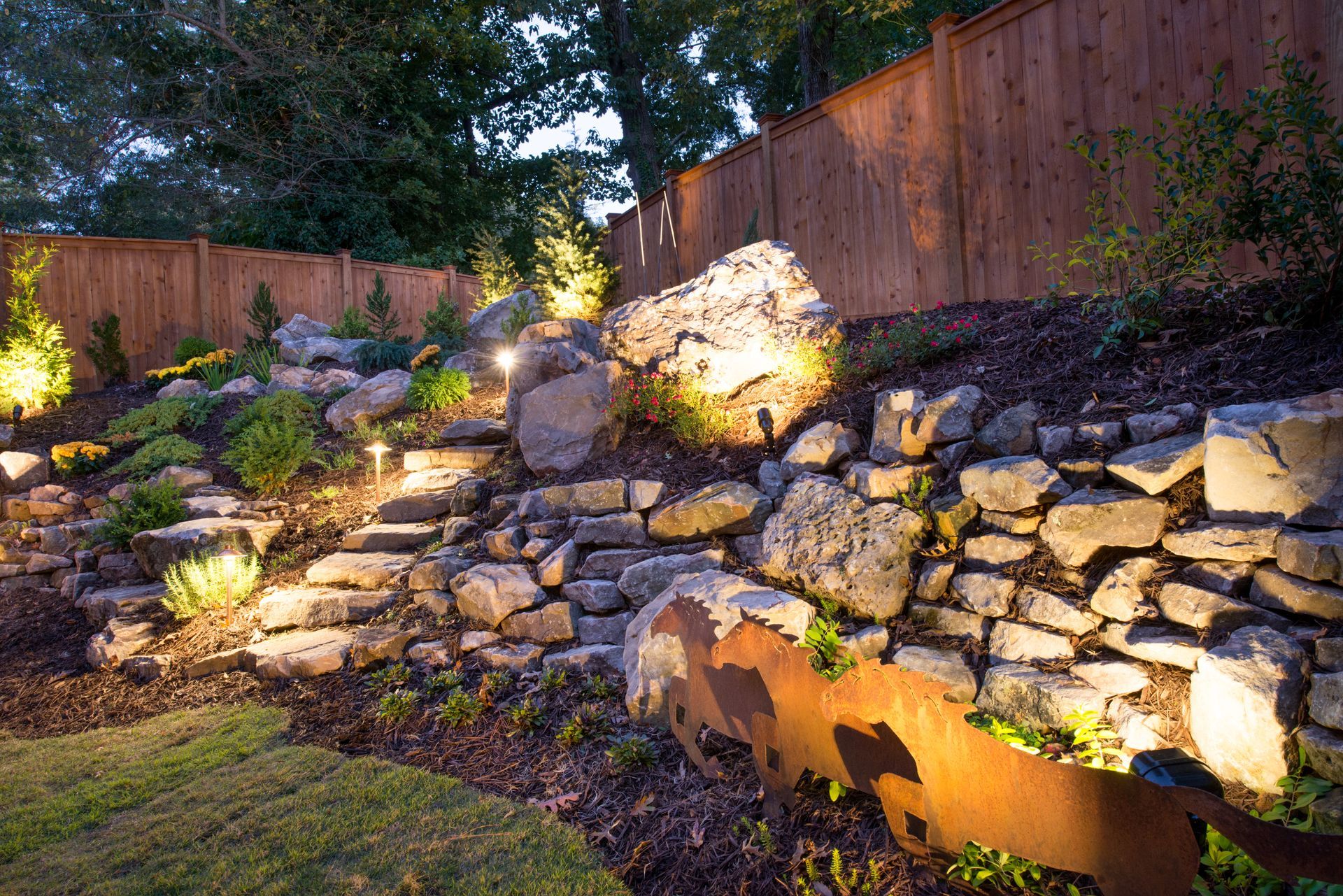 A rock wall with lights on it and a wooden fence in the background.