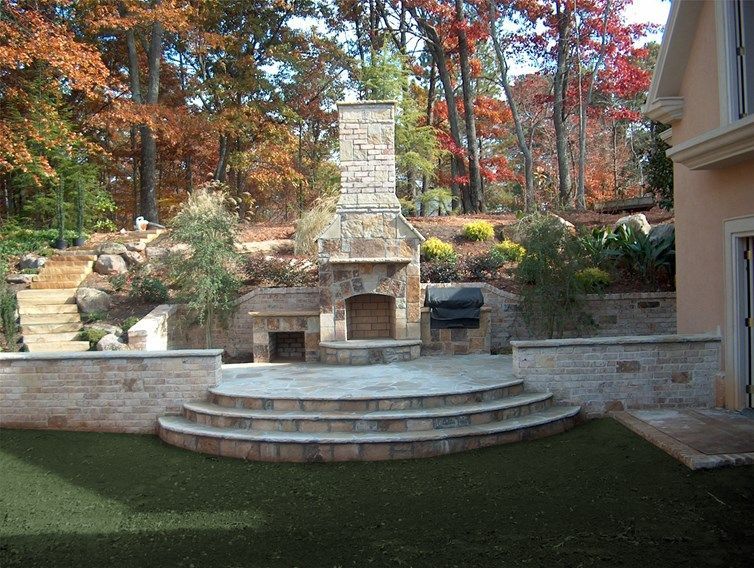 A backyard with a stone fireplace and brick stairs and patio hardscape