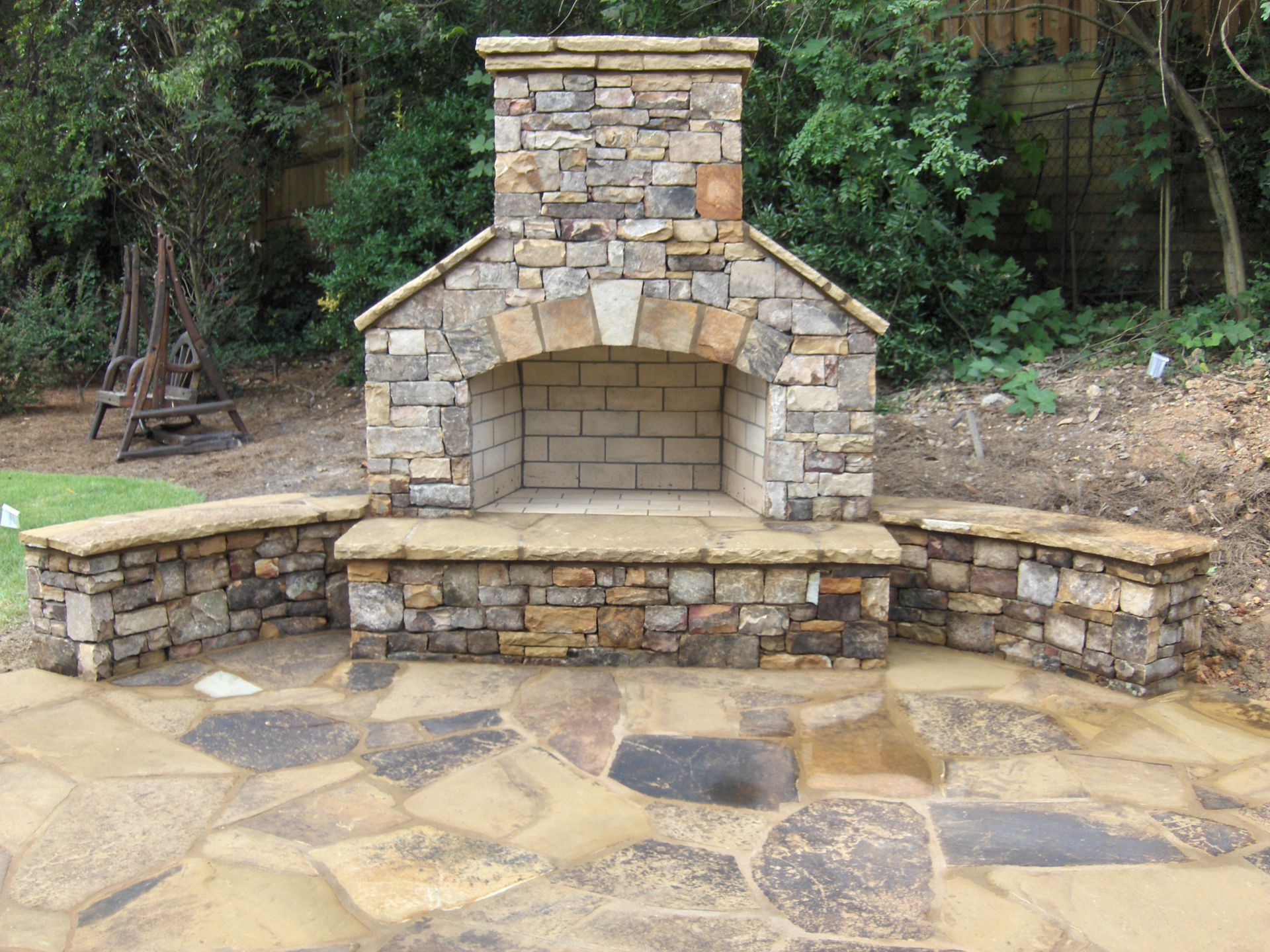 A stone fireplace is sitting in the middle of a stone patio.