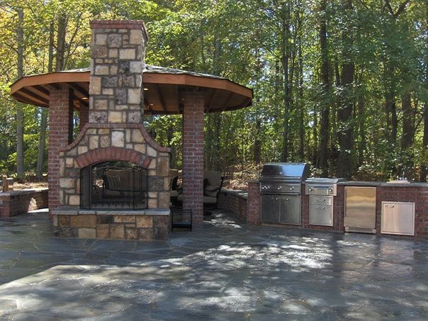 A brick fireplace surrounded by trees and a grill