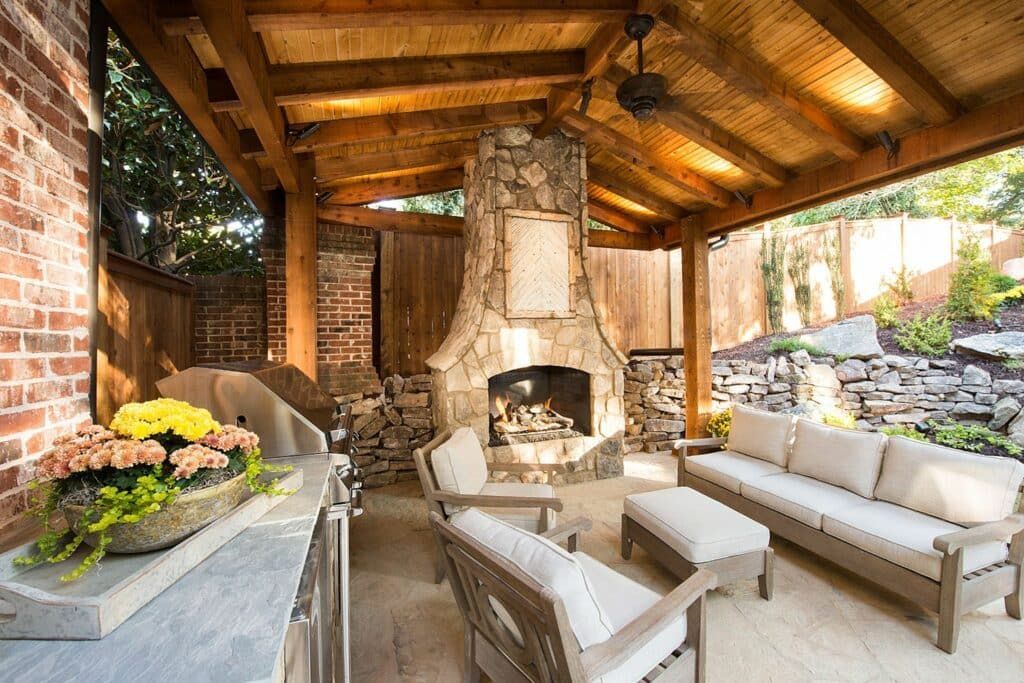 A patio with a fireplace , couch , chairs and a ceiling fan.