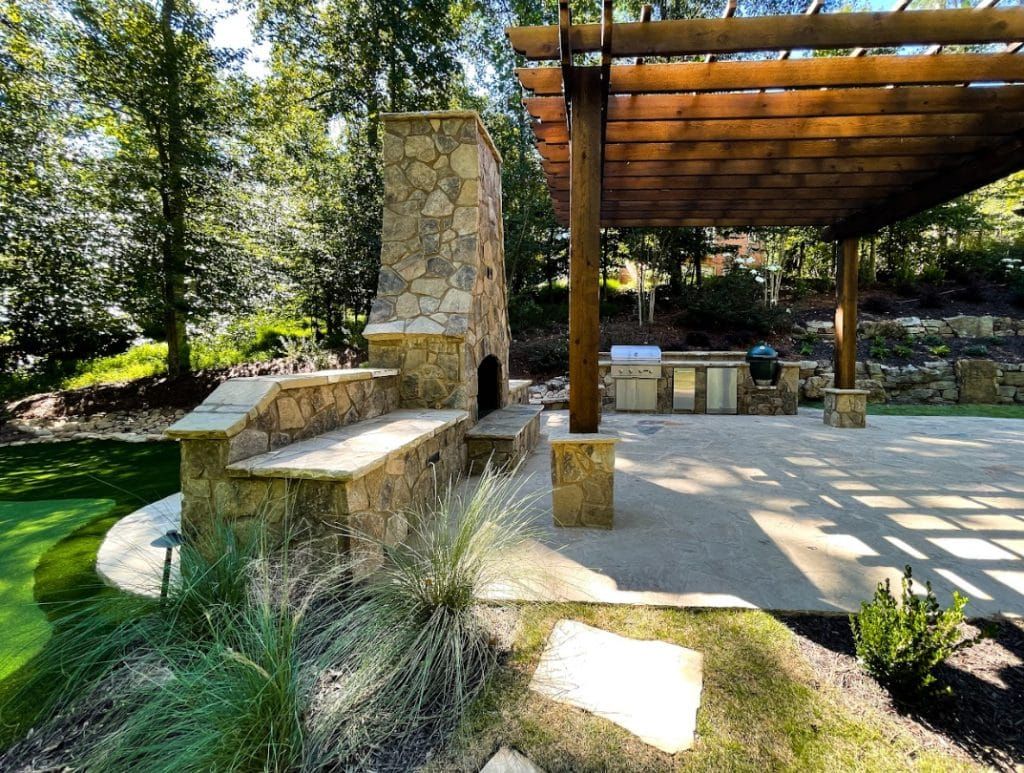 A patio with a stone fireplace and a wooden pergola.