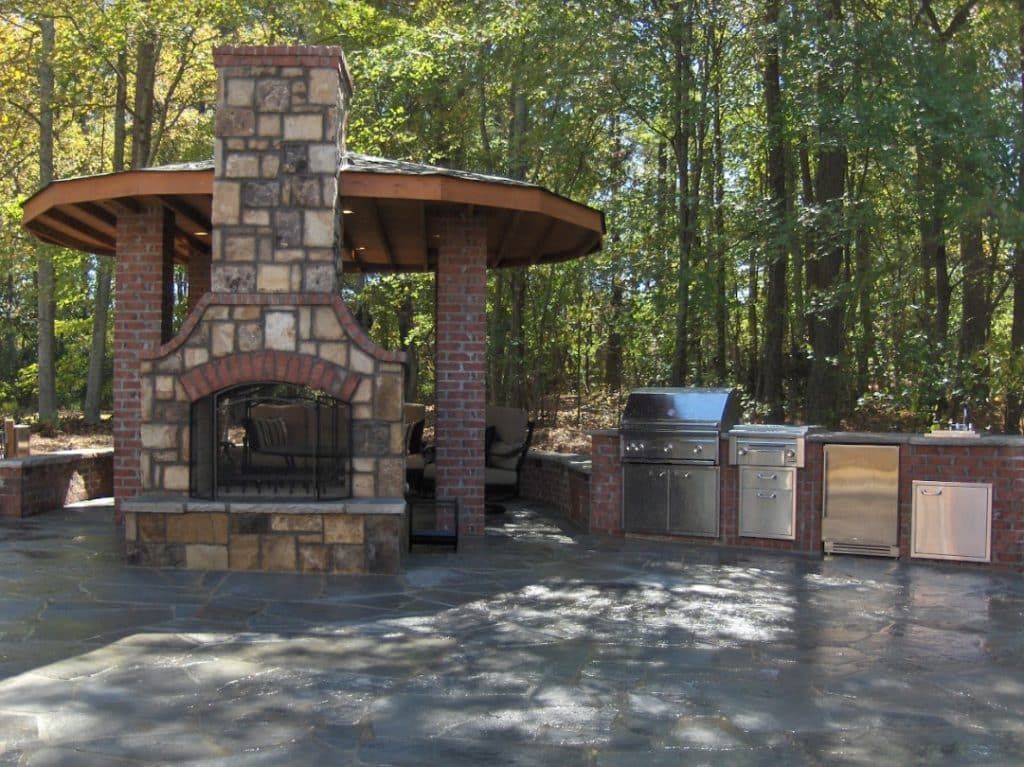 An outdoor kitchen with a brick fireplace and a grill