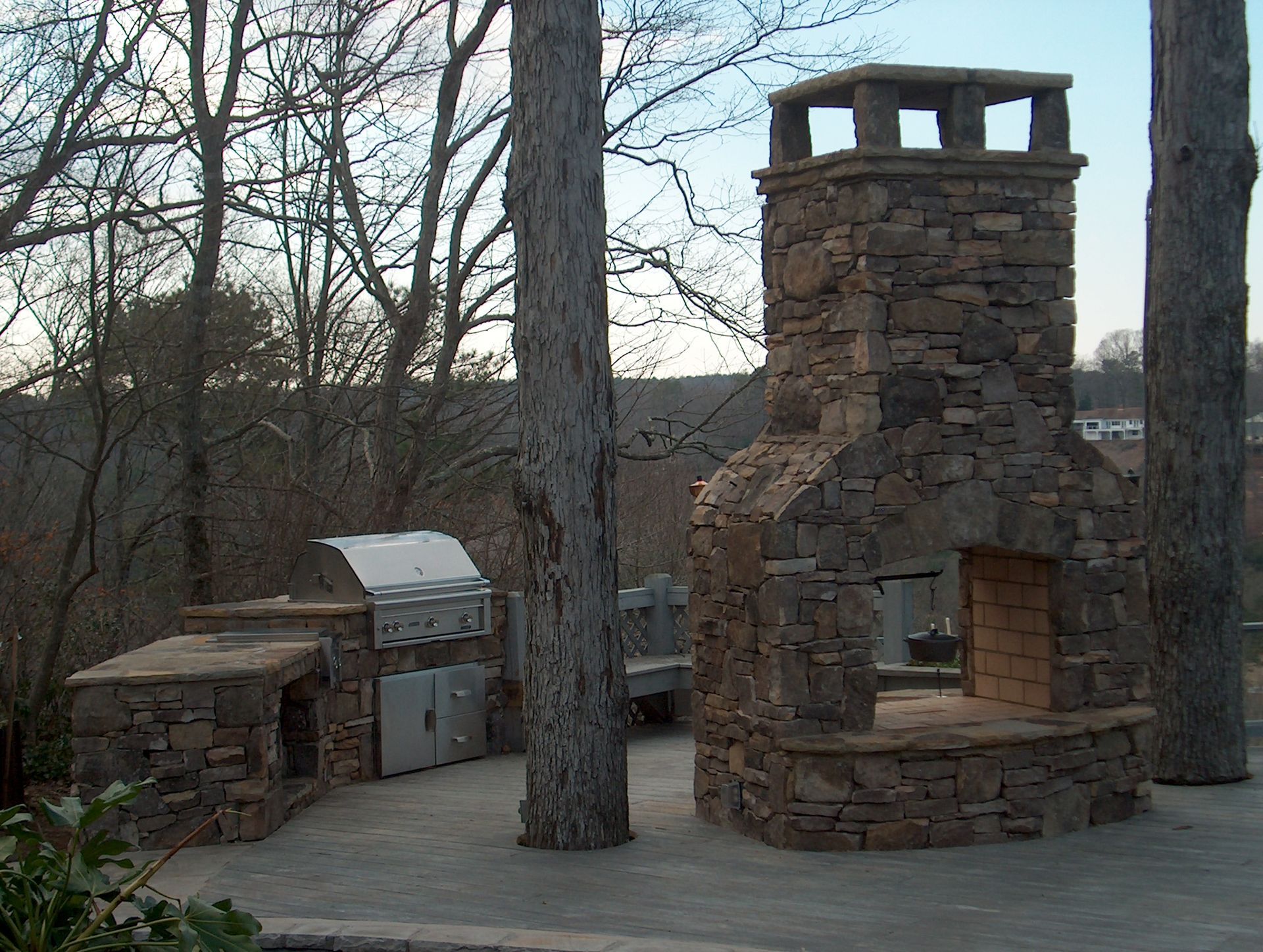 A stone fireplace is surrounded by trees and a grill