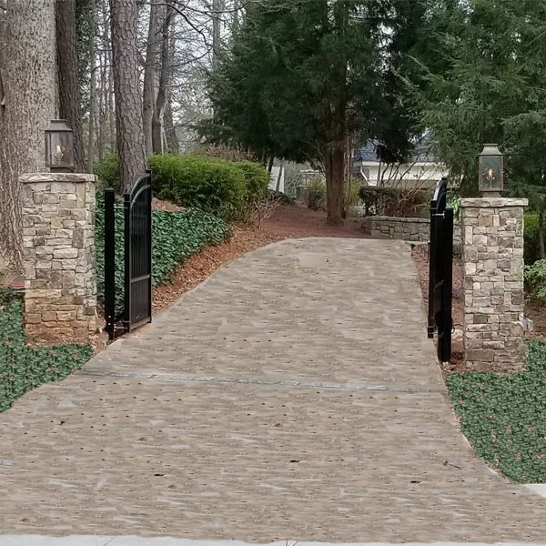 A brick driveway with a gate and stone pillars entranceway leading to a house.