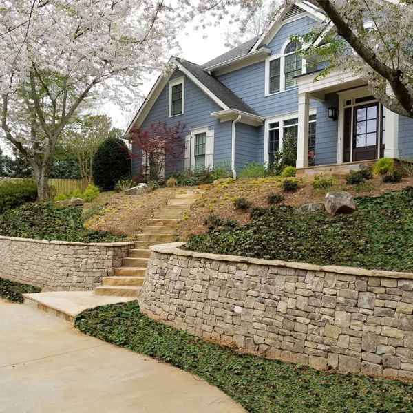 A blue house on a hill with a stone retaining wall in front of it