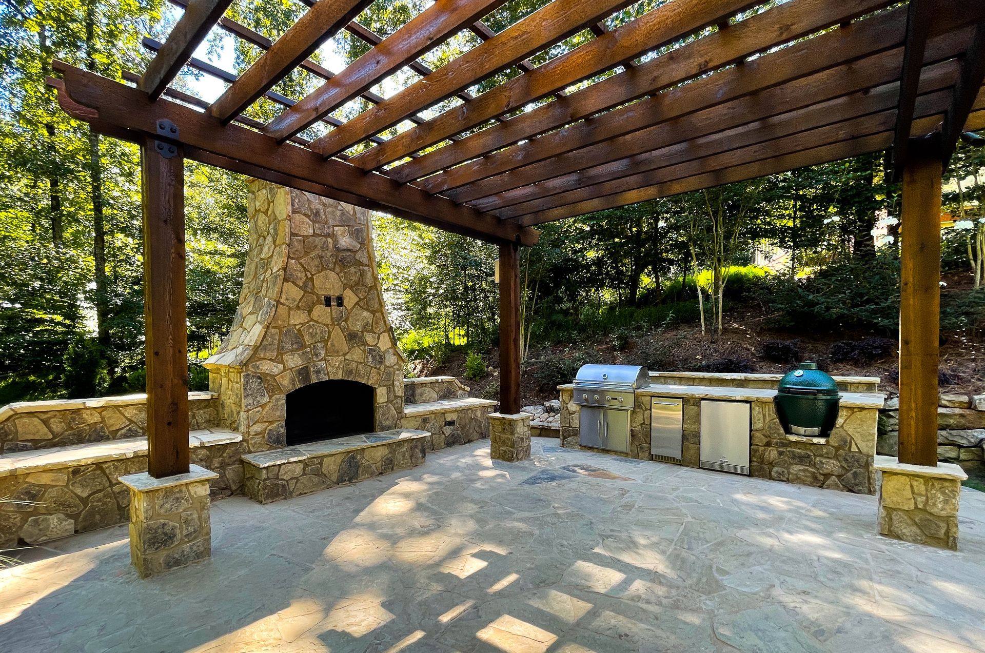 A patio with a wooden pergola and a stone fireplace and outdoor kitchen in Sandy Springs, GA..