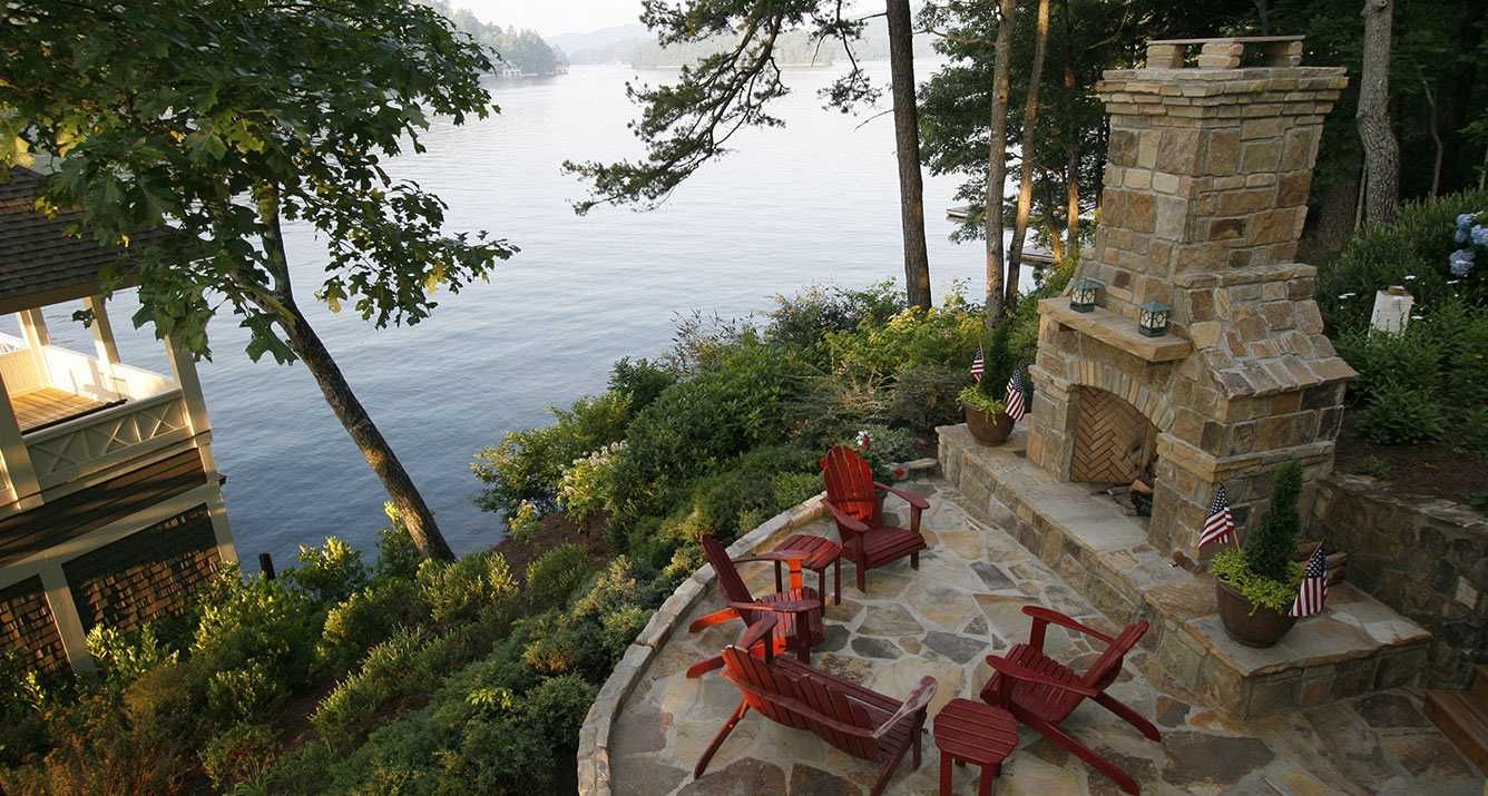 A patio with chairs and a fireplace overlooking a lake.