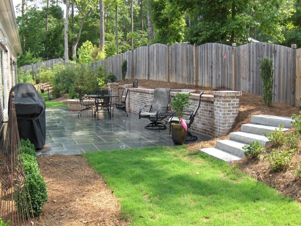 A backyard with a patio and stairs and a wooden fence.