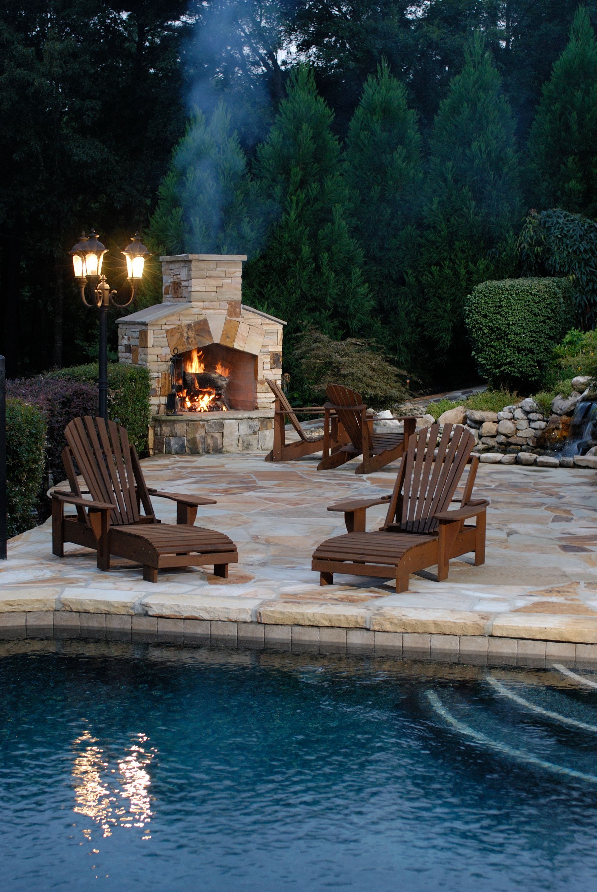 A patio with chairs and a fireplace next to a pool