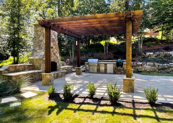A stone patio with a pergola and an outdoor fireplace and outdoor kitchen in the backyard.