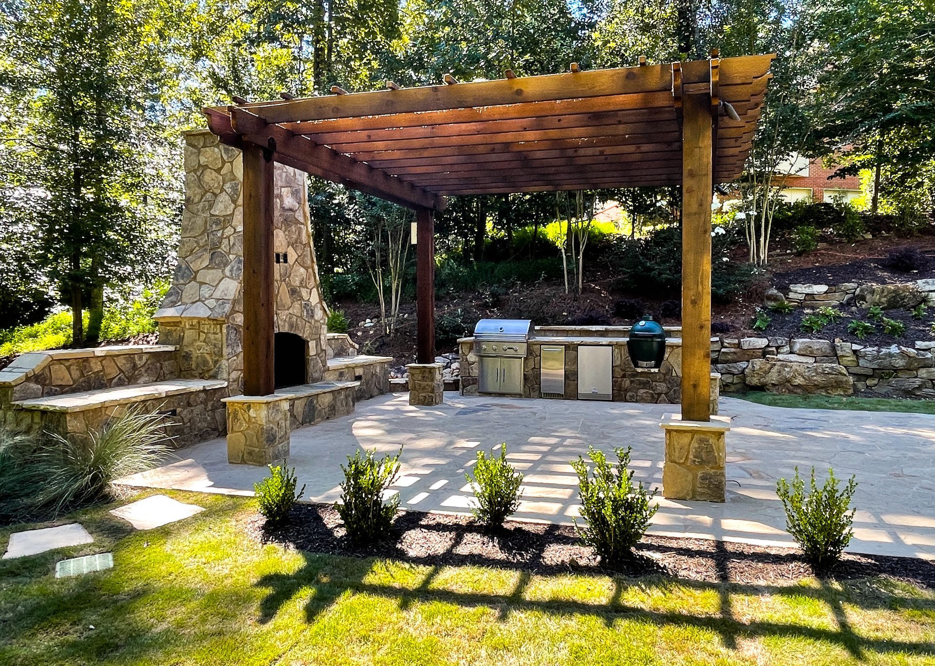 A wooden pergola over a patio with a grill and fireplace.