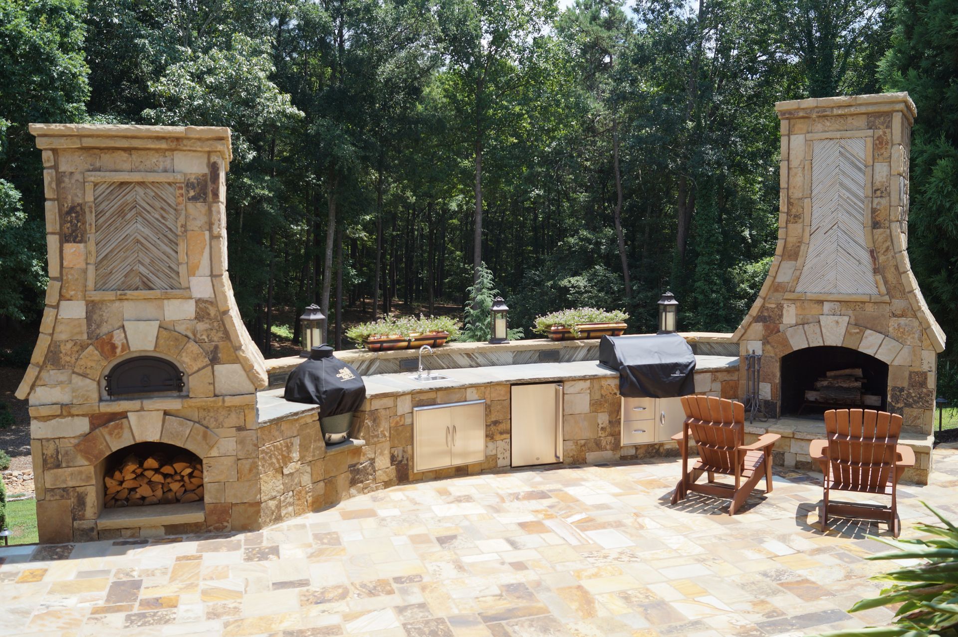 A patio with two stone fireplaces and chimneys and a grill outdoor kitchen