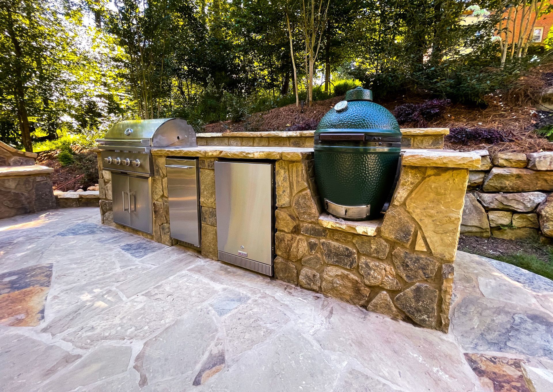 A large green egg grill is sitting on top of a stone wall.