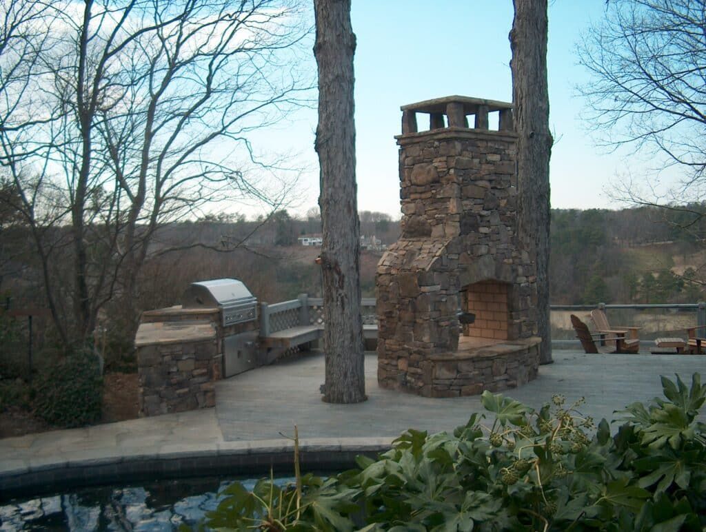 A stone fireplace is surrounded by trees and a swimming pool