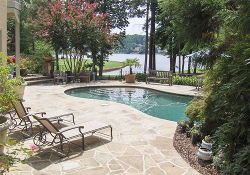 A large swimming pool is surrounded by a stone patio and chairs.