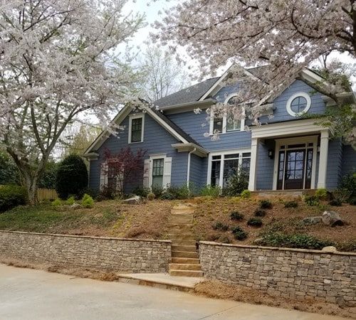 A blue house with cherry blossom trees in front of it.
