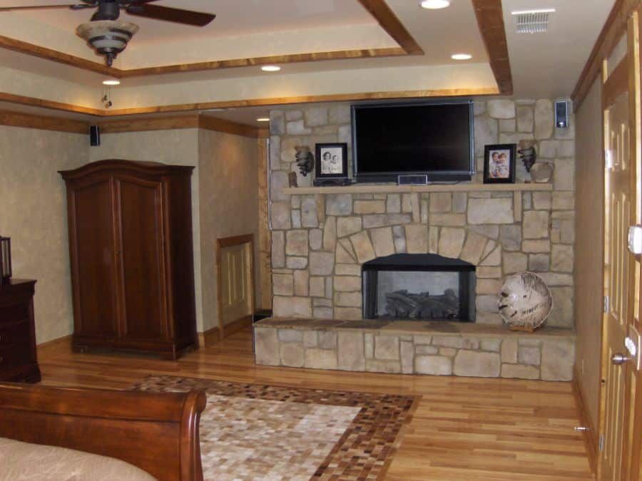 A bedroom with a stone fireplace and a flat screen tv