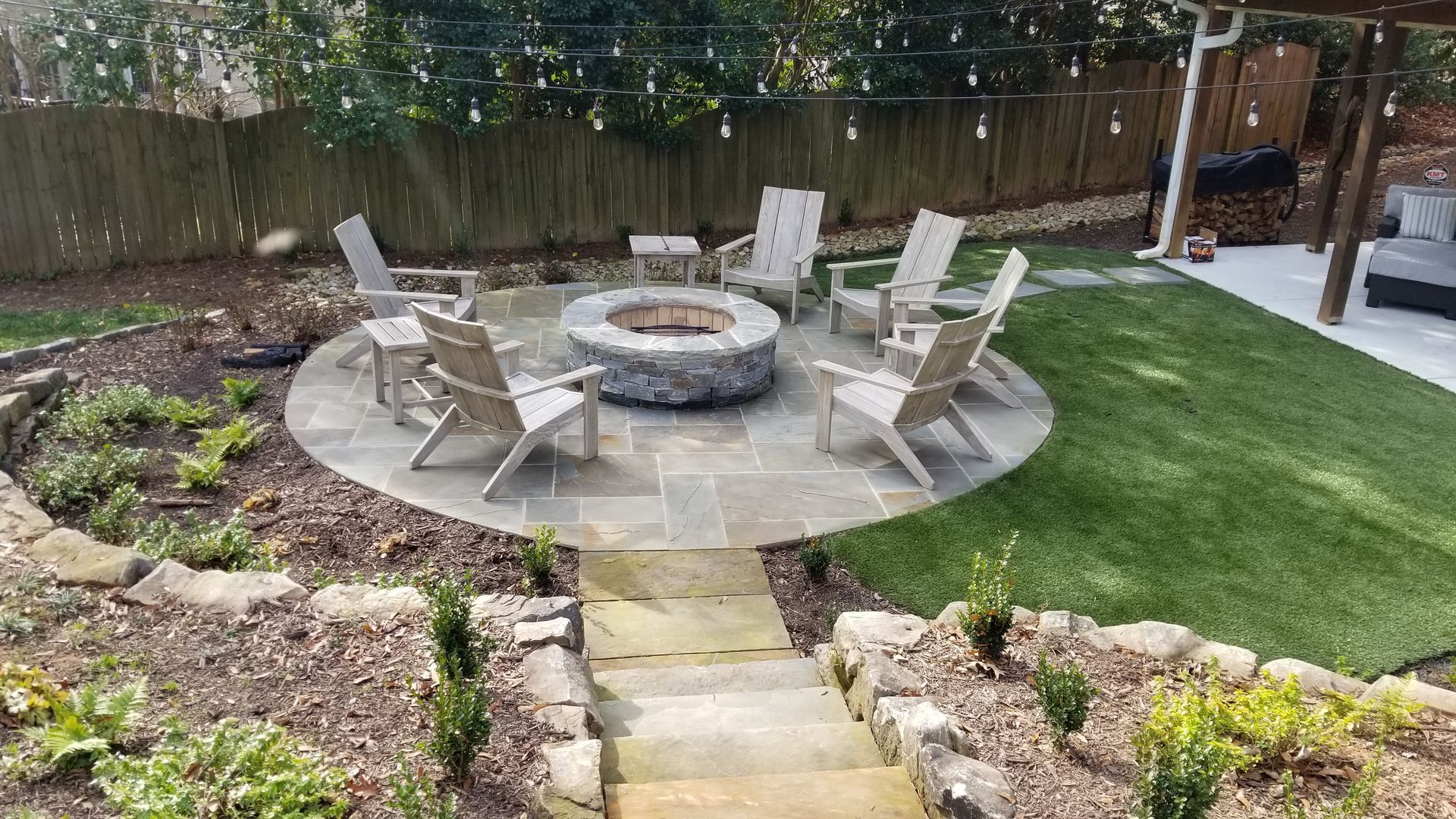 There is a fire pit in the middle of the backyard surrounded by chairs.