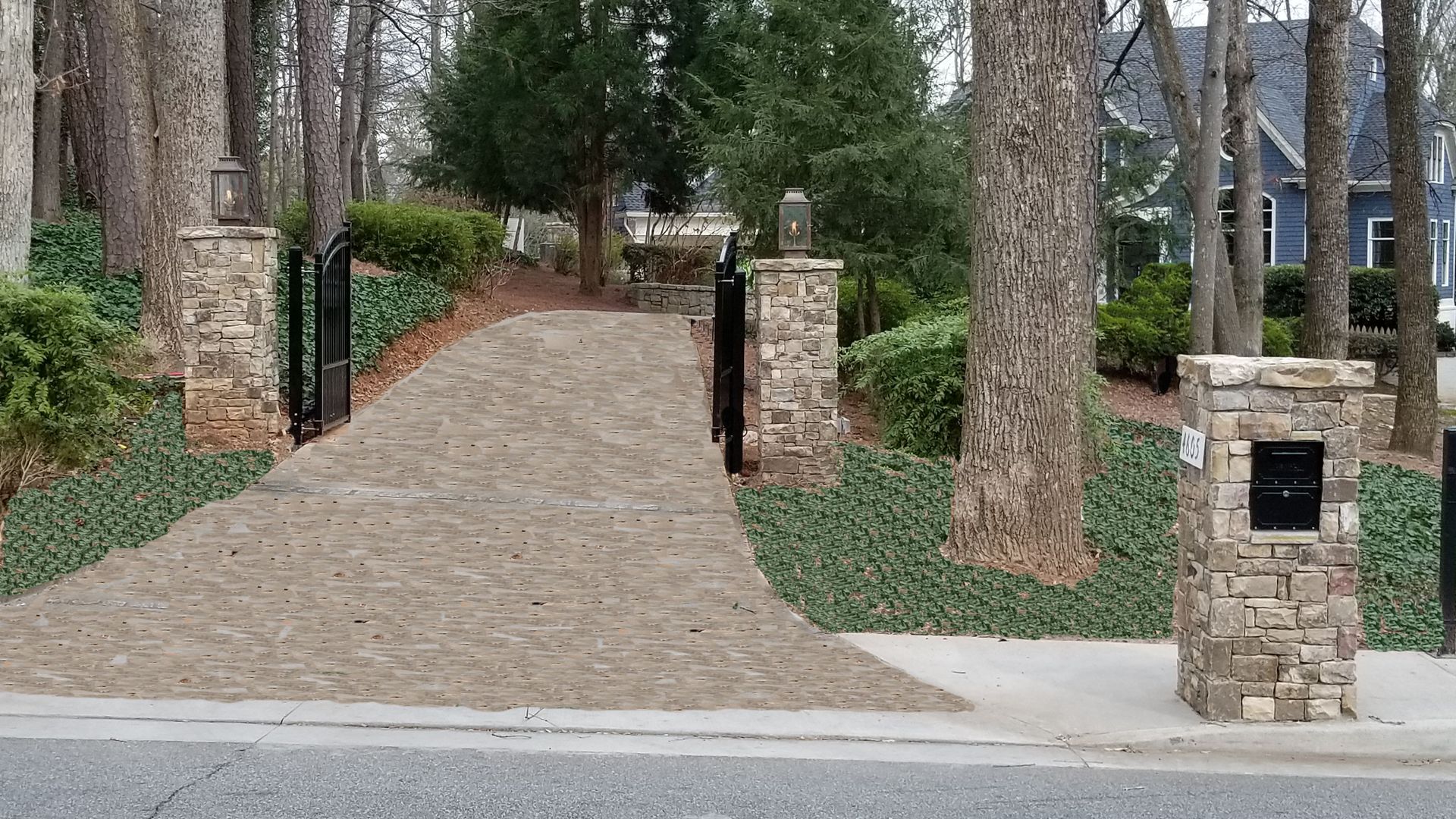 A driveway leading to a house surrounded by trees and stone columns and stone mailbox.