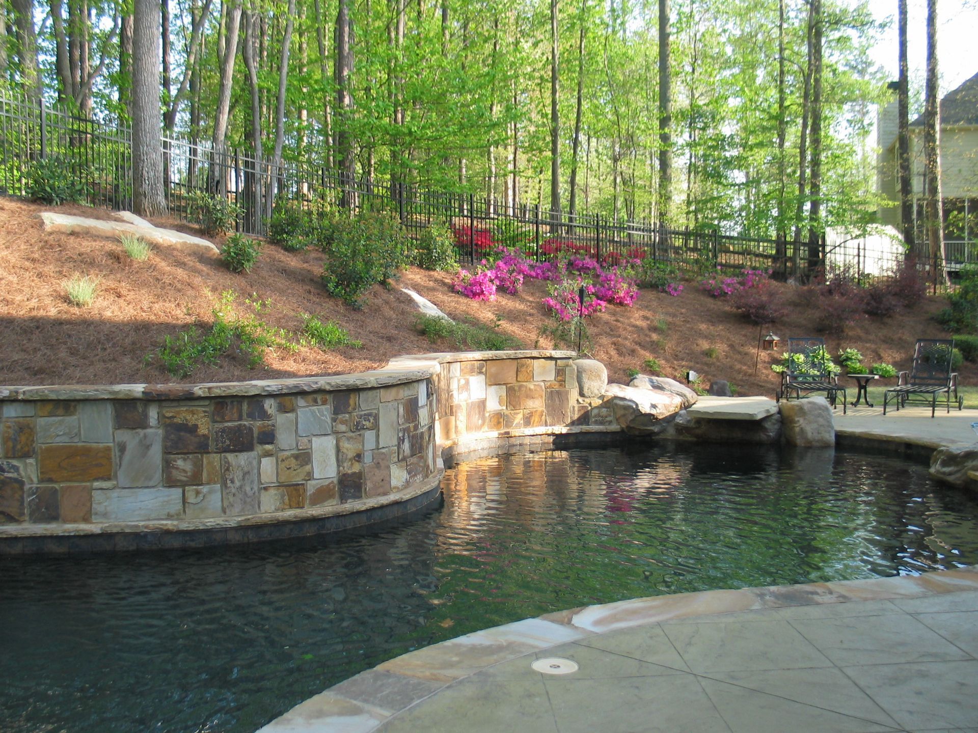 A swimming pool with a stone wall and trees in the background