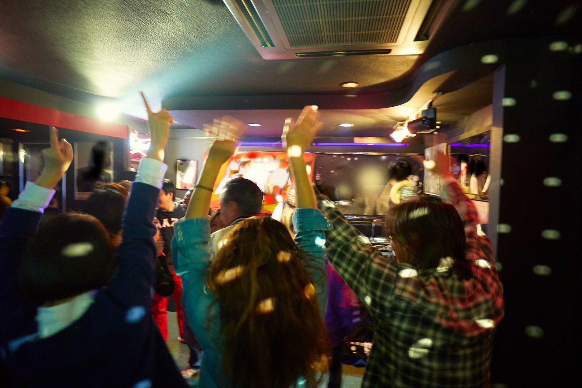 A group of people are dancing in a club with their arms in the air.