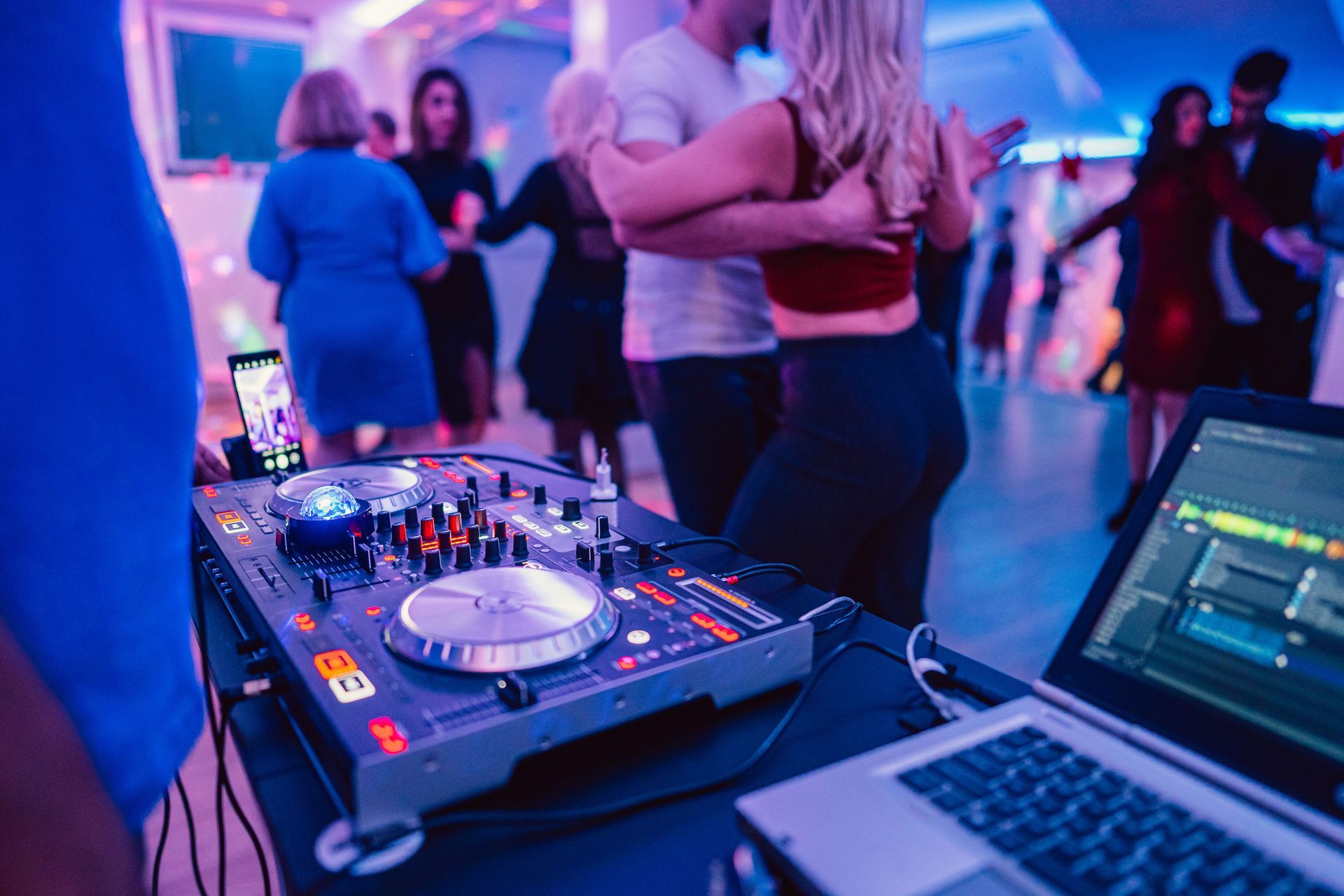 A dj is playing music at a party with people dancing in the background.