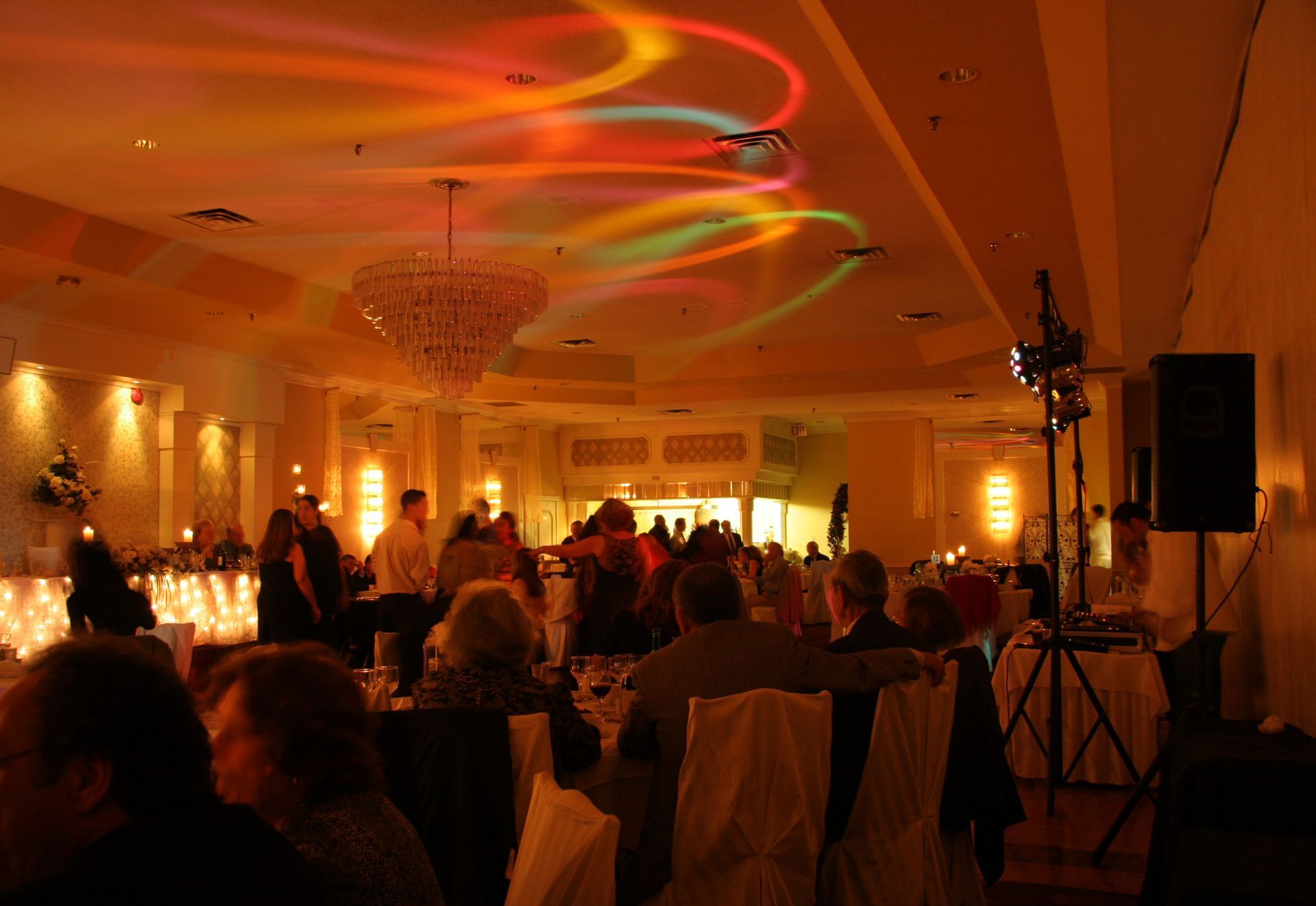 A group of people are sitting at tables in a large room with colorful lights on the ceiling.