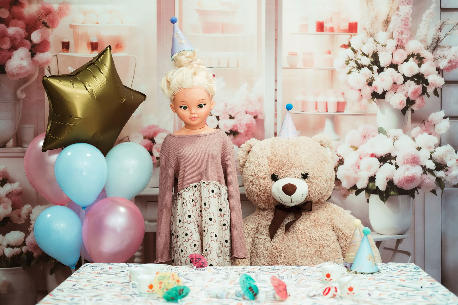 A doll and a teddy bear are sitting at a table with balloons.