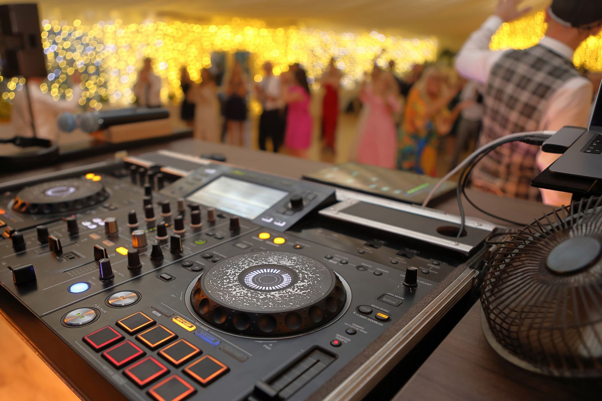 A dj is playing music at a party with a crowd of people dancing in the background.