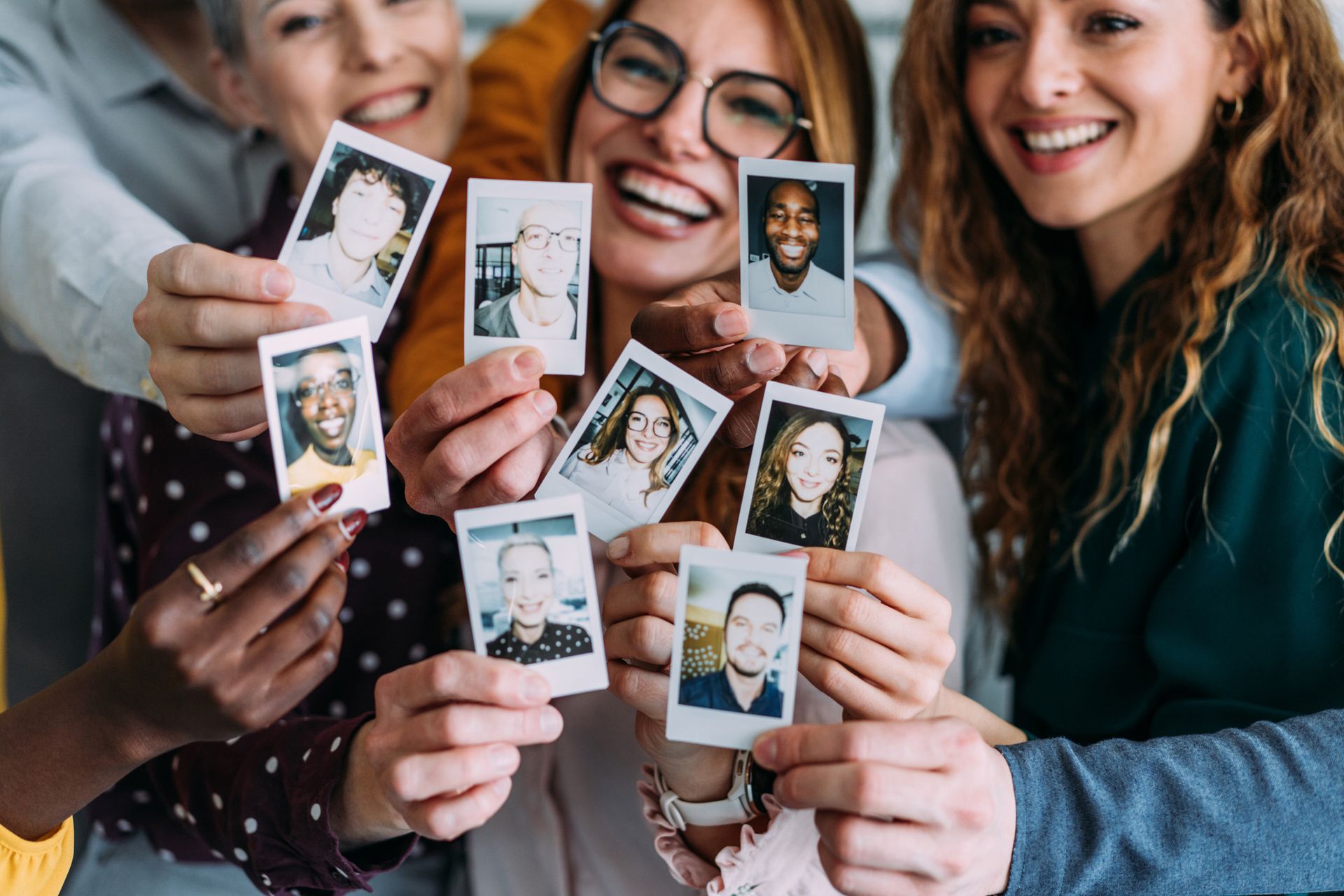 A group of people are holding up polaroid pictures of themselves.
