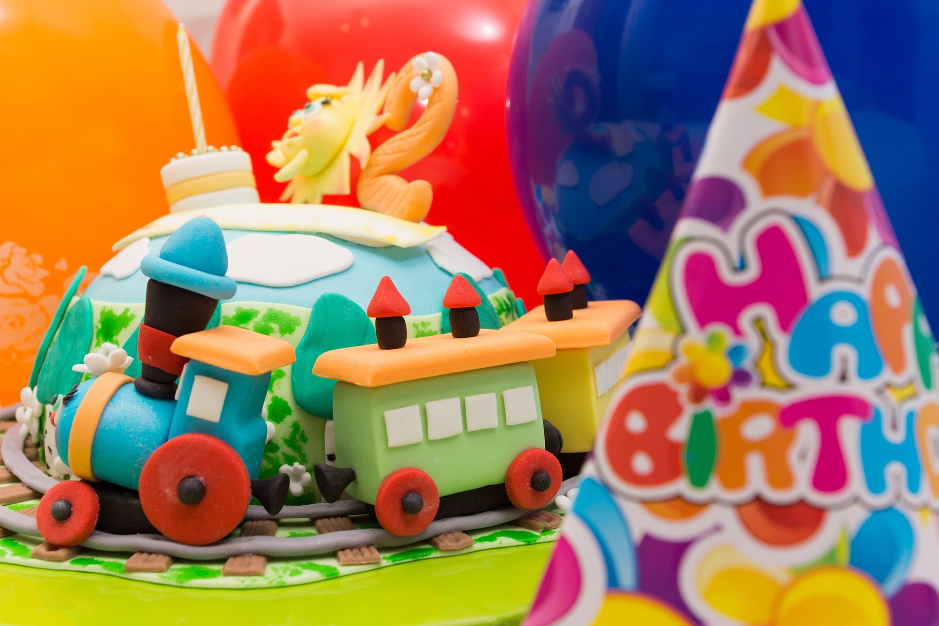 A birthday cake with a train on it and balloons in the background.