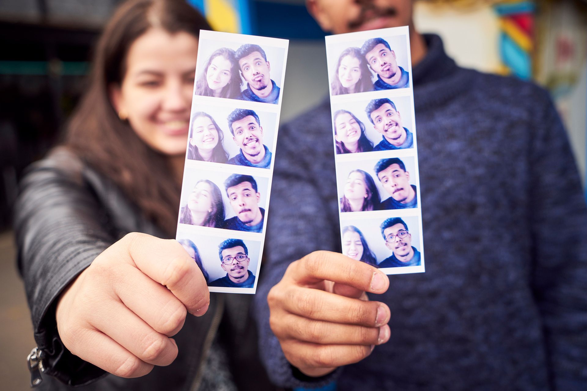A man and a woman are holding up a pair of photo booth strips.