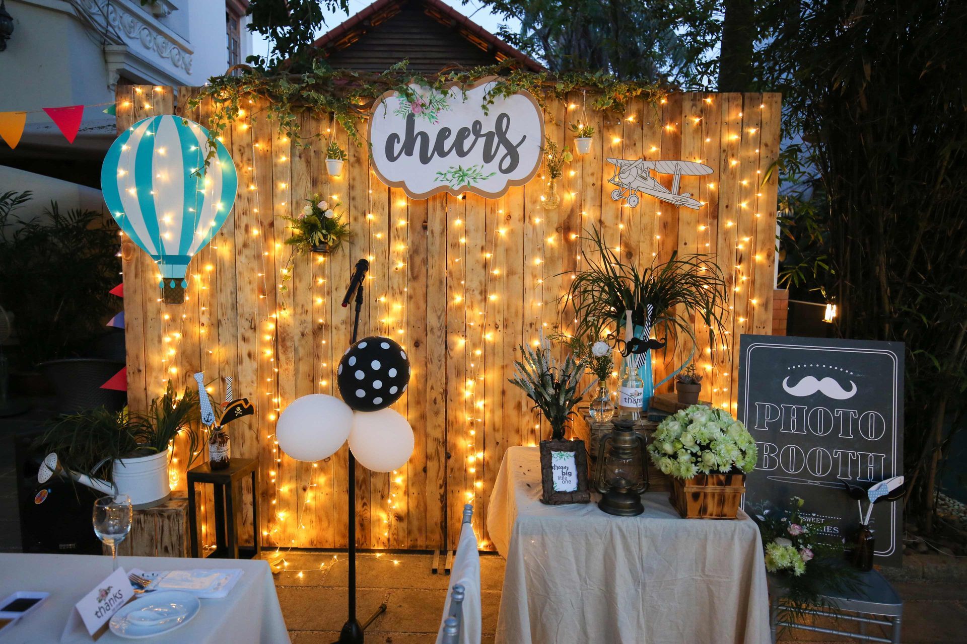 A wooden wall with lights and balloons and a table in front of it.
