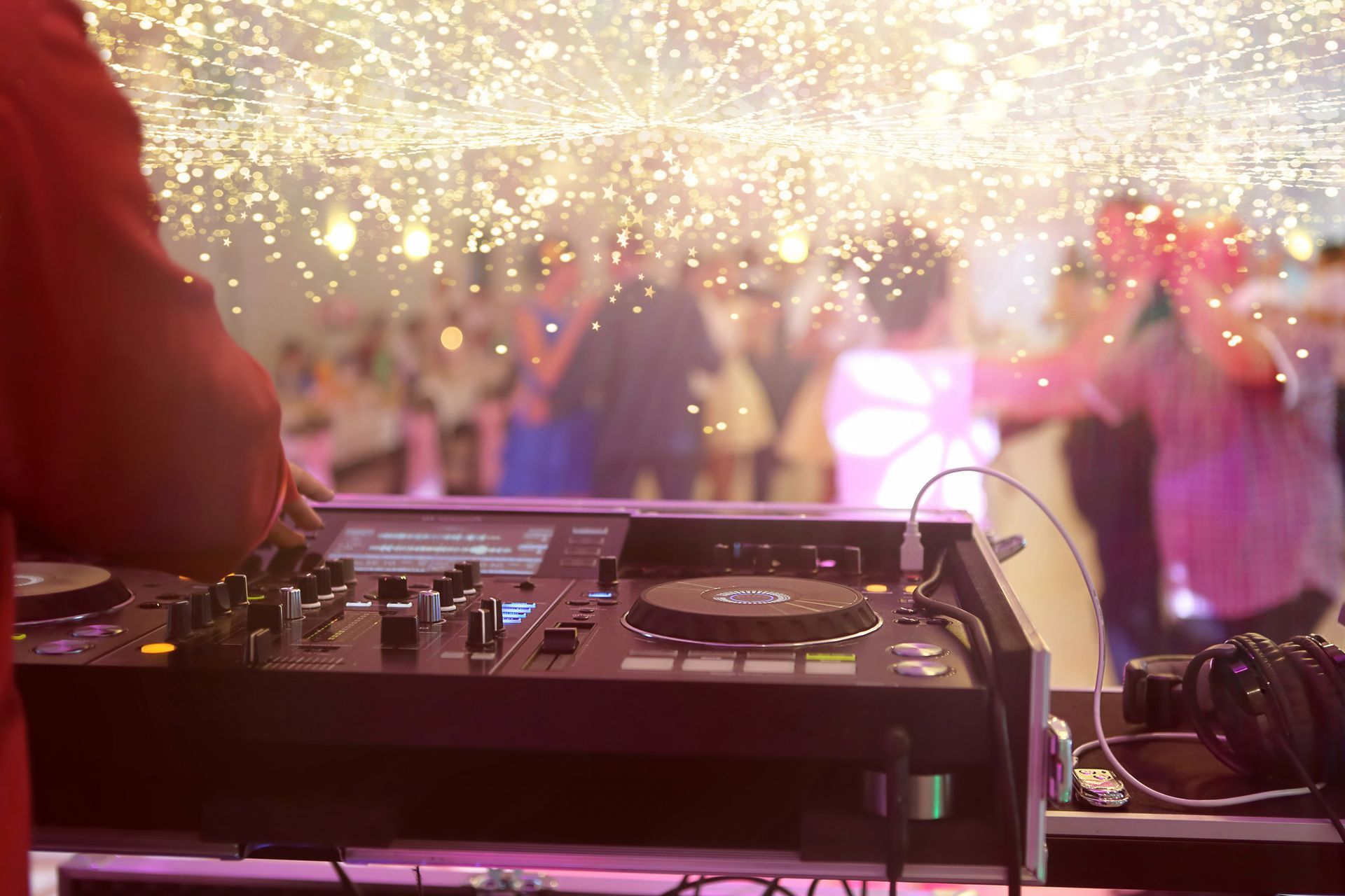 A dj is playing music at a party with a crowd of people dancing in the background.