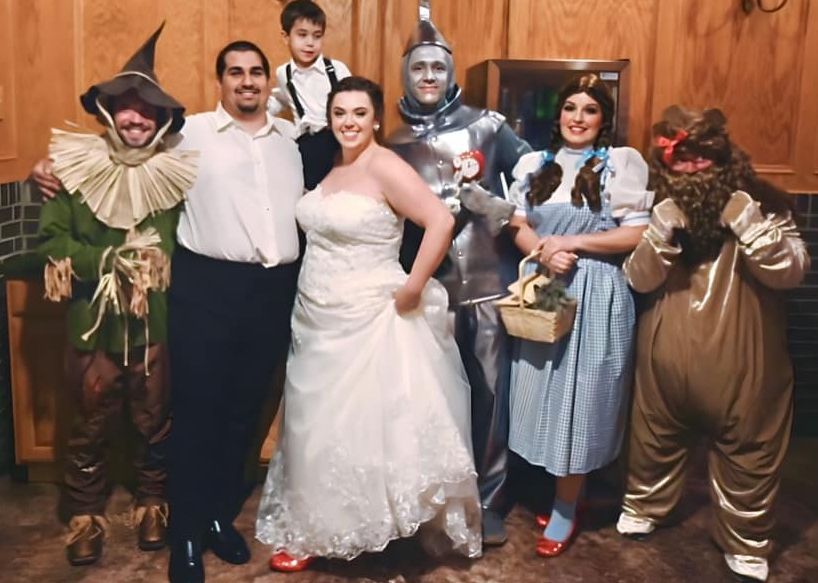 A bride and groom pose for a picture with wizard of oz characters.