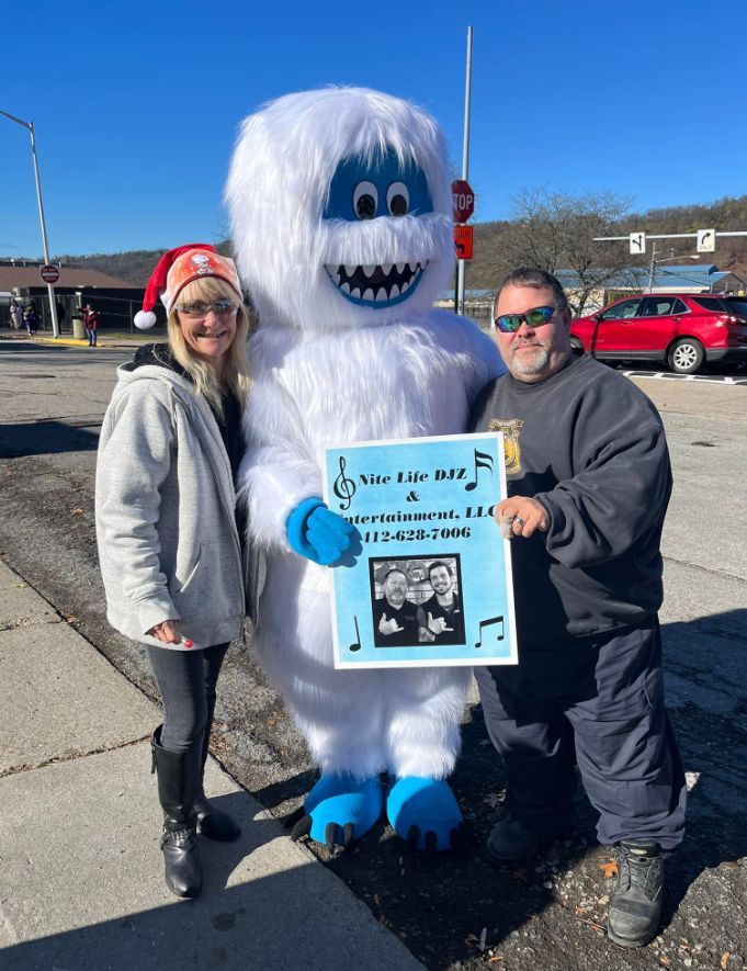 A man and a woman are standing next to a yeti mascot holding a sign.