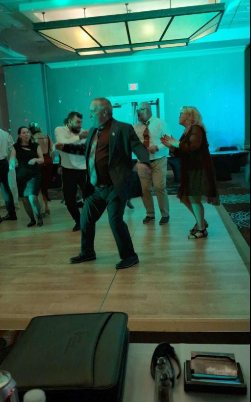 A group of people are dancing on a wooden floor in a room.