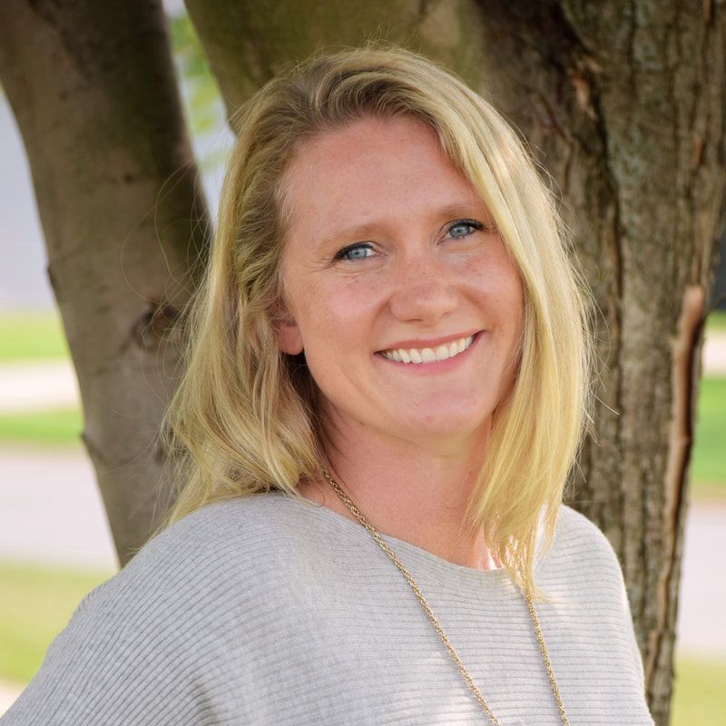 A woman is smiling for the camera while standing next to a tree.