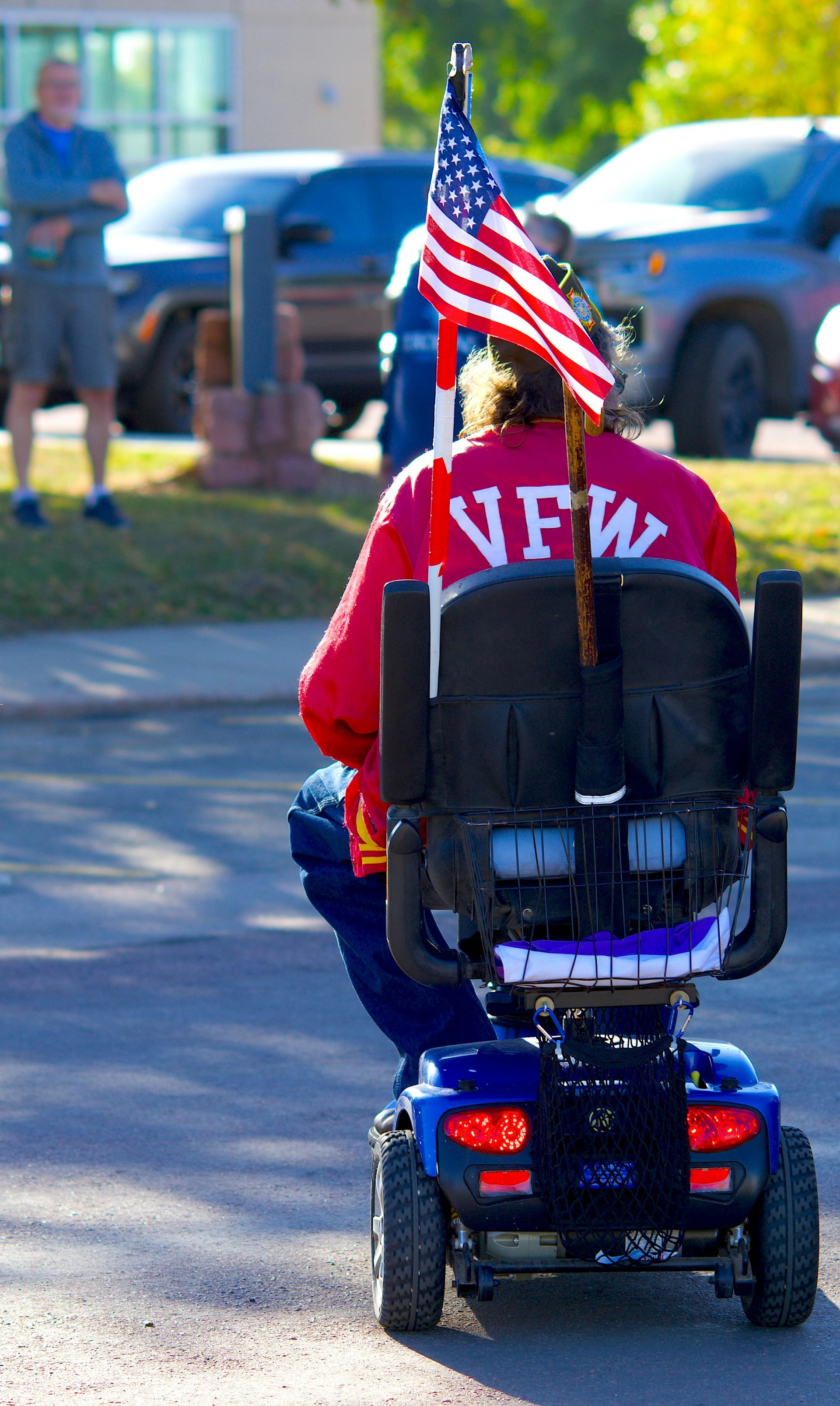Person in a red shirt rides a mobility scooter with an American flag attached, outdoors on a sunny day