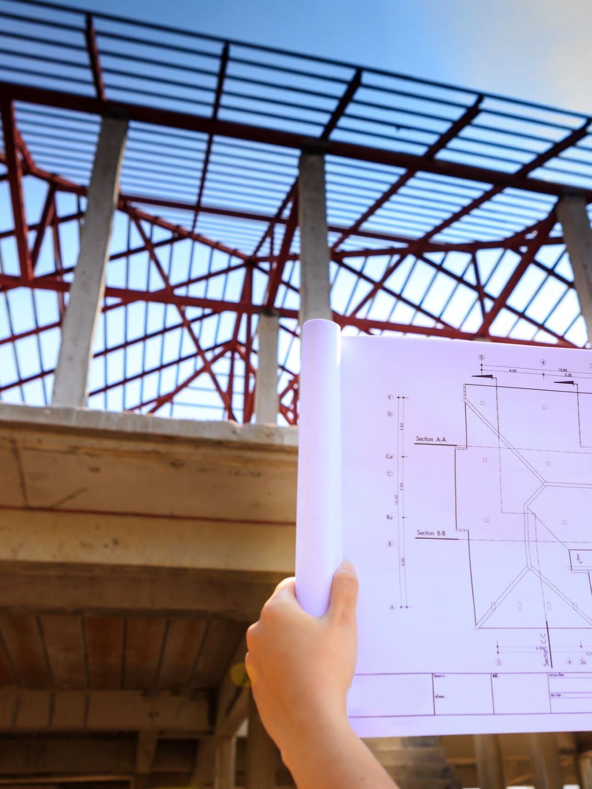 A Person Is Holding A Blueprint In Front Of A Building Under Construction — GEO – AM Consulting In Lismore, NSW