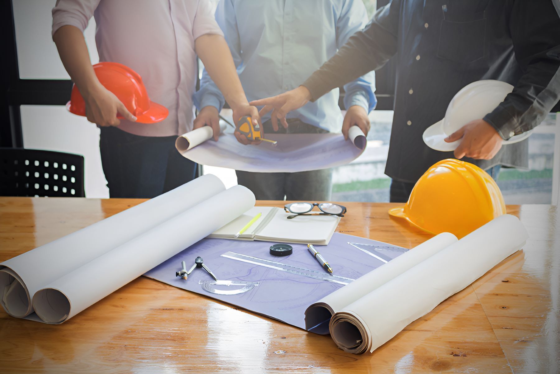 A Group Of Engineers Are Looking At A Blueprint On A Wooden Table — GEO – AM Consulting In Lismore, NSW