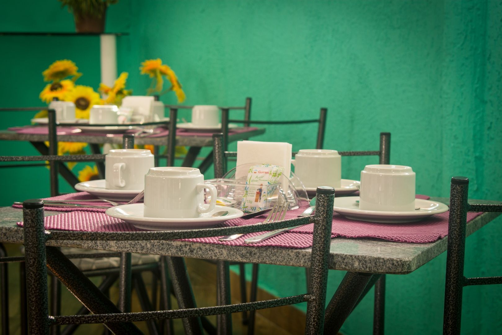 Uma fileira de mesas com xícaras e pires em um restaurante.