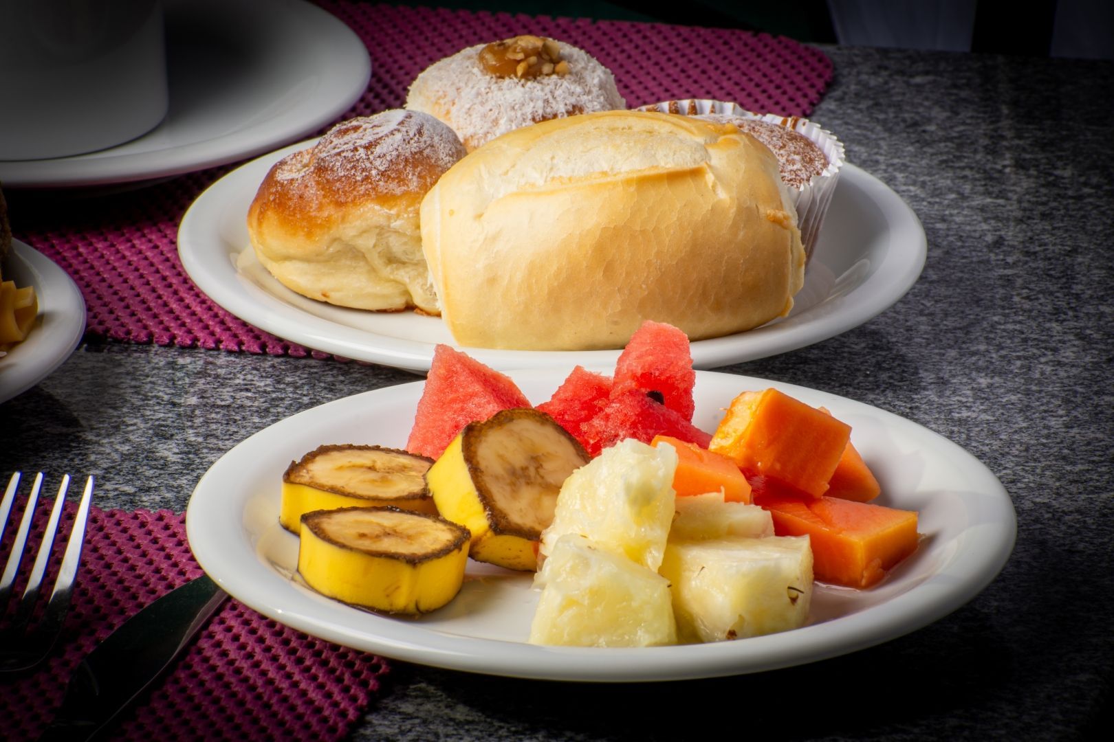 Um prato de frutas e pão sobre uma mesa com um garfo.