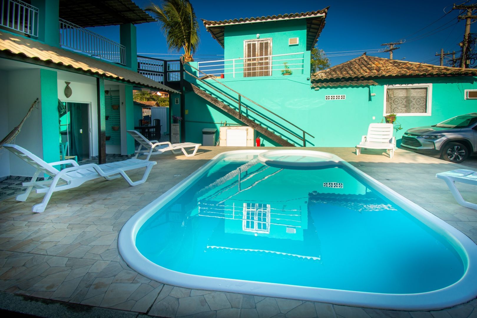 Uma grande piscina fica em frente a uma casa verde.